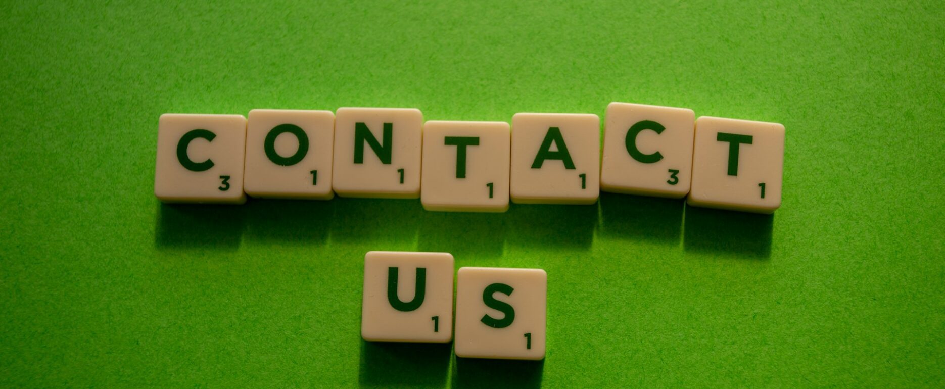 Scrabble tiles spelling out "Contact Us" on a wooden surface